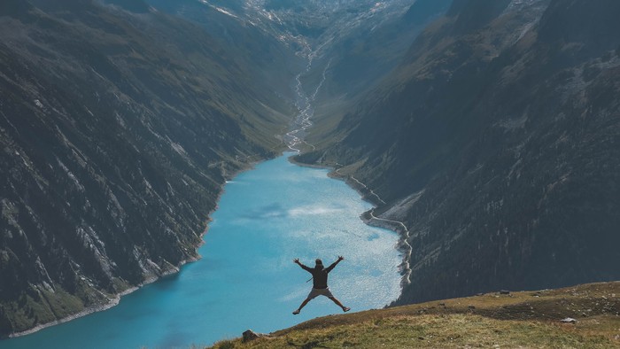 Person springt vor atemberaubender Berglandschaft mit blauem See.