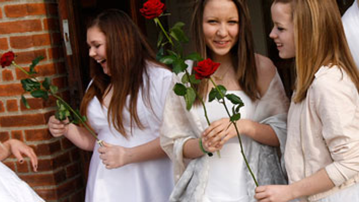 En gruppe piger i hvide klæder holder røde roser.