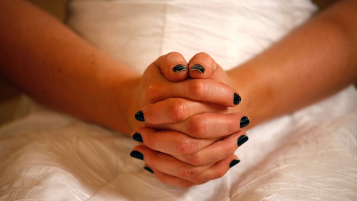 En person holder håndene sammen med mørke nagler og smykke på fingrene.