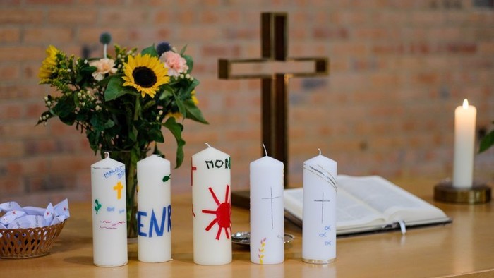 Kerzen mit Namen und Symbolen, Blumen, Kreuz und Buch auf dem Tisch