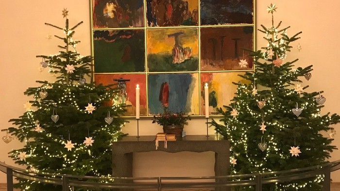 To skønnede juletræer med lys og pynt foran et farverigt maleri