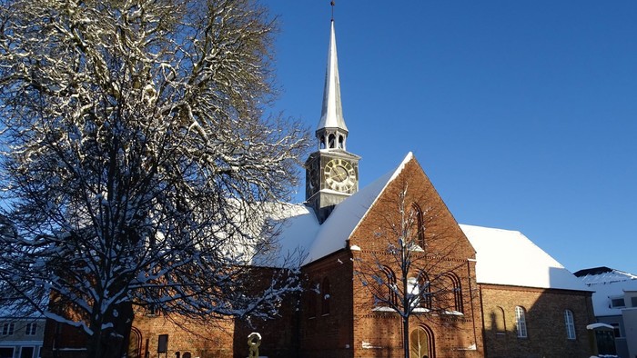 En snede kirke med klokketårn og en især snebelagt træ foran