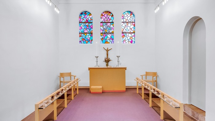 En lille kapel med farverige vinduesglas, alter med krucifix og tre stolene foran
