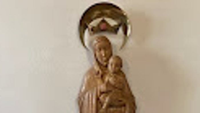 Auf dem Bild ist eine Statue der Jungfrau Maria neben zwei Topfpflanzen auf einem Tisch zu sehen.