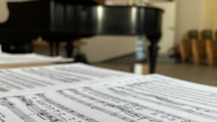 Notenblätter auf einem Tisch neben einem Flügel in einem gemütlichen Raum ausgebreitet.