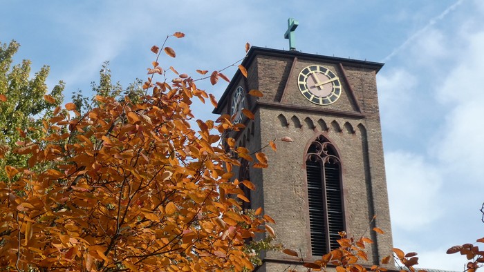 Herbstblätter vor Kirchturm mit Uhr