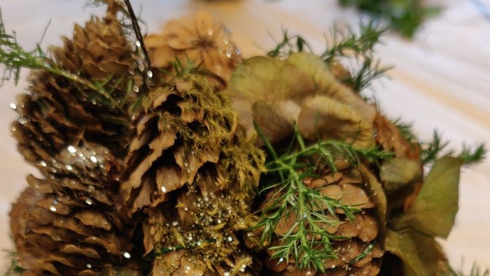 En pyntel af tørre nåletrækerner og grønne planter i en lille metallkande.