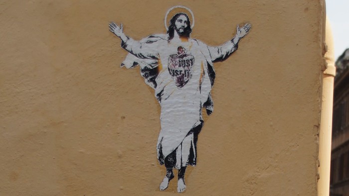 Ein Bild einer Person an einer gelben Wand über Kopfsteinpflaster.