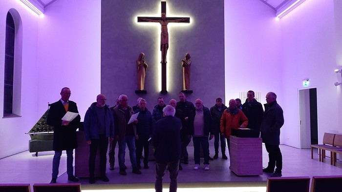 Eine Gruppe von Menschen singt in einer Kirche vor einem Kreuz.