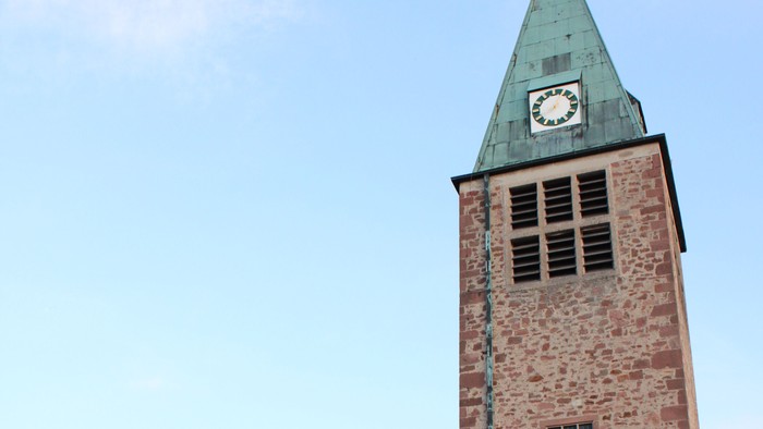 Steinerne Kirche mit hohem Uhrturm und bogigem Eingang.