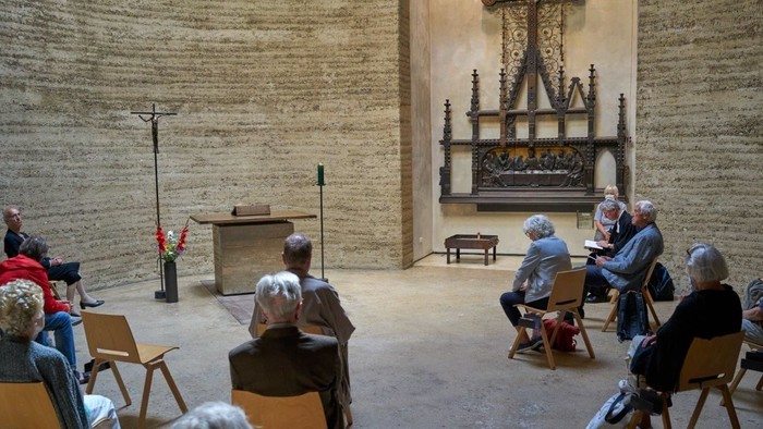 Eine Gruppe älterer Menschen sitzt in einem Raum mit steinernen Wänden und hört einem Redner zu.