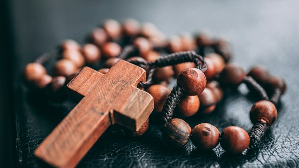 Ein hölzernes Kreuz liegt auf einer Kette aus Holzperlen