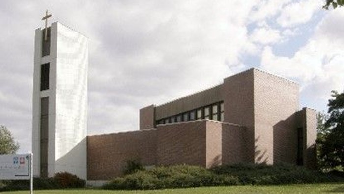 Das Bild zeigt eine moderne Kirche mit hohem Turm und Ziegelmauerwerk auf einem grünen Rasen.