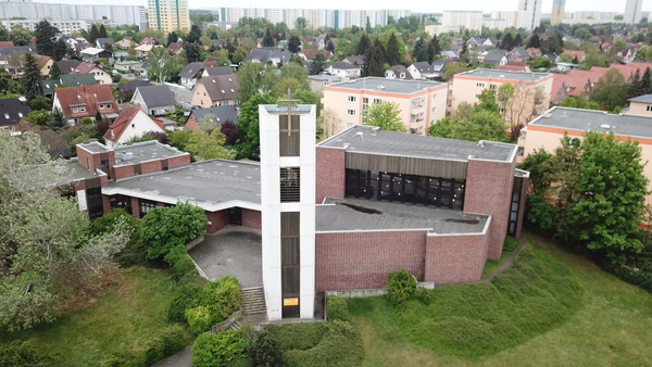 Ein modernes Kirchengeb�ude mit hohem Kreuz inmitten von Gr�nfl�chen und Wohnh�usern.