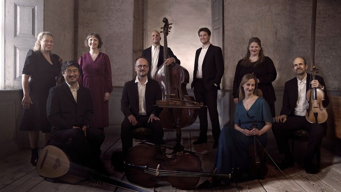 Et klassisk musikensemble poserende sammen med forskellige instrumenter i en elegant indendørs indstilling.