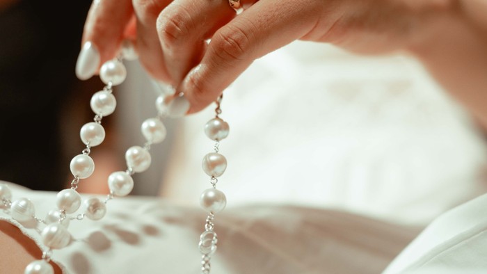 Nahaufnahme der Hand einer Braut, die eine Rosenkranzkette hält.