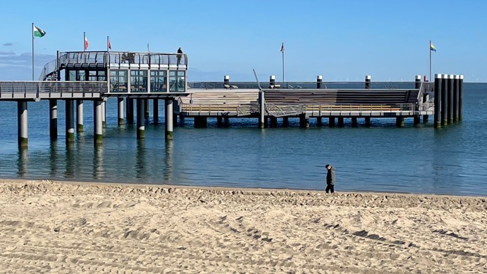 Ein Pier ragt in den Ozean, mit einer einsamen Person am Strand.