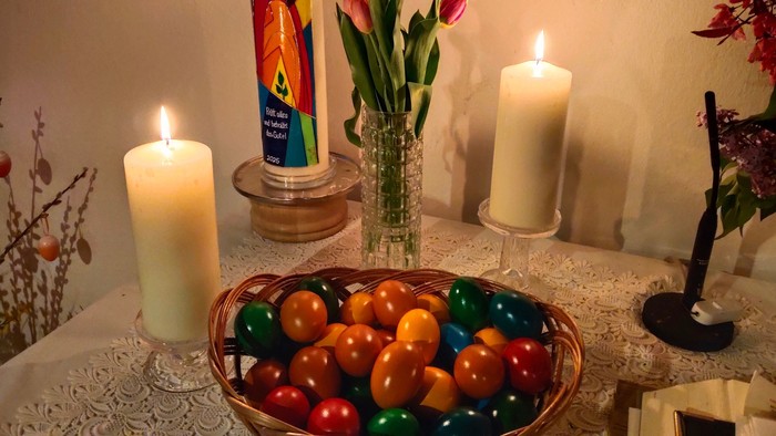 Ein Tisch mit brennenden Kerzen, einer Vase mit Tulpen und einer Schale mit bunten Eiern