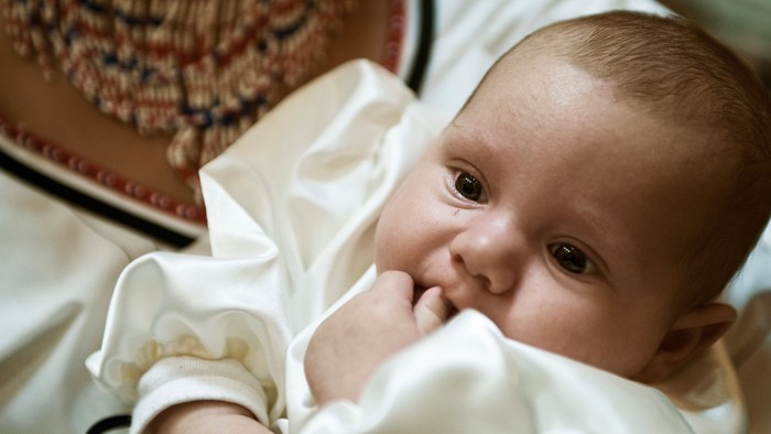 Et spæd barn ligger i en hvid dopant, med en mors halskæde i baggrunden