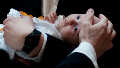 En person holder et spæd barn, der ser op og er omklædt i en hvid og gule tekstil.