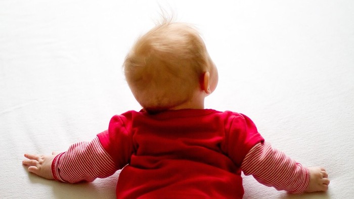 Ein Baby liegt auf dem Bauch auf einem weißen Teppich.