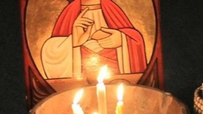 En lysstake med tre lys foran et billede af Jesus