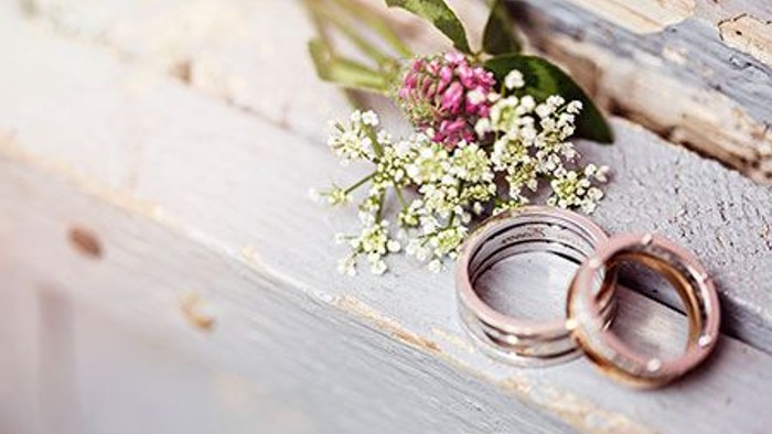 Zwei goldene Ringe und eine kleine Blumenanordnung auf einem Holzbalken