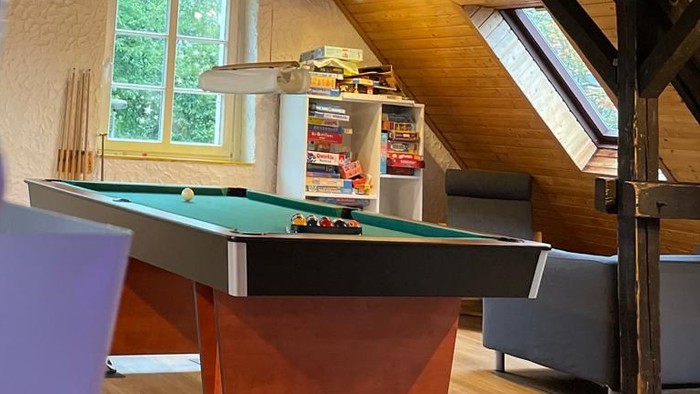 Ein Spielzimmer mit Billardtisch und Sofa unter schrägen Holzbalken