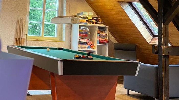 Ein Spielzimmer mit Billardtisch und Sofa unter schrägen Holzbalken