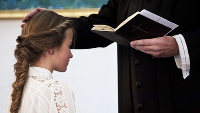 En kvinde med frisyr og hvid blouse ser op på en bog holdt af en mand i mørkt tøj.