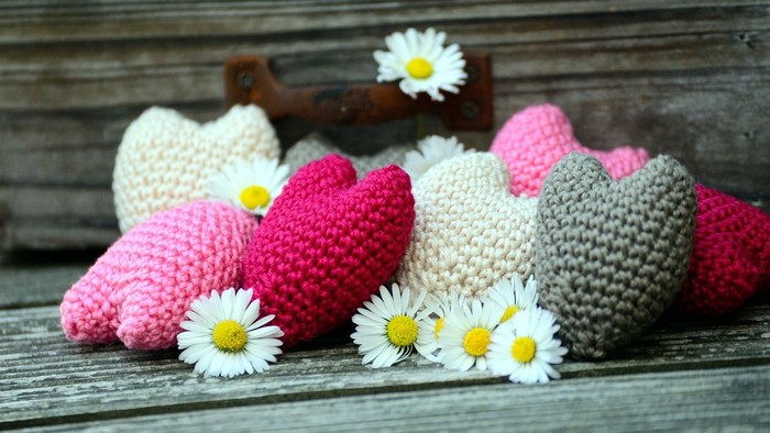 Syv hjerteformede strikkede figurer og tre margeriter på træ.