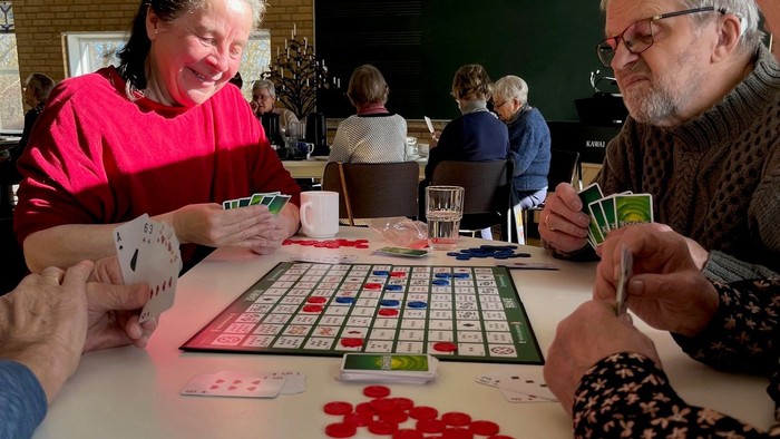 En gruppe ældre spiller Scrabble og kortspil på en bord.