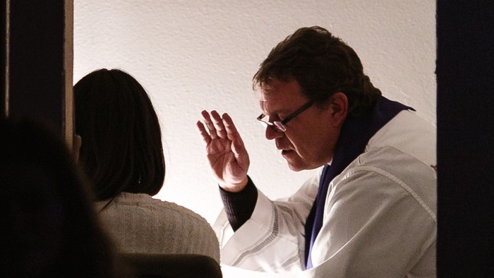 Ein Mann in weißem Anzug winkt auf einer Bühne.