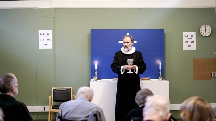 En præst står ved alteret og holder en tale i en kirke.