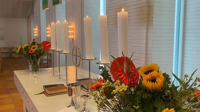 Bord med blomster, lysstake og brød i lys og farverig kirke