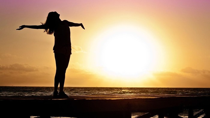 woman staring at sunrise with arms out wide
