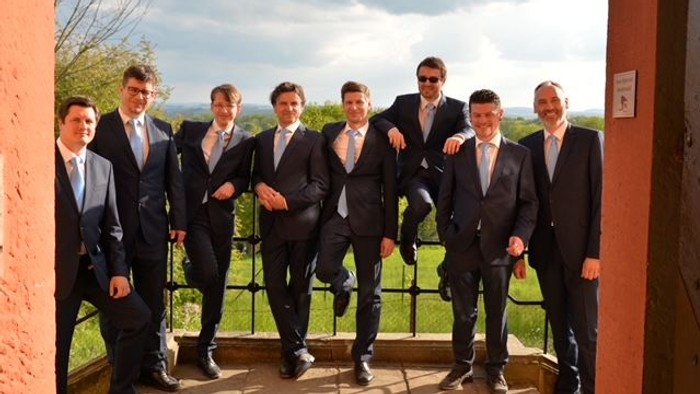 Eine Gruppe von Männern in Anzügen posiert vor einem Tor.