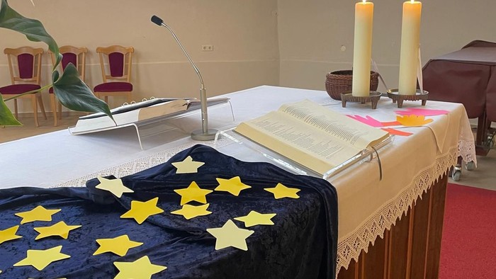 Eleganter Kirchenaltar, geschmückt mit einem blau sternförmig gemusterten Tuch, Kerzen und geöffneten Gesangbüchern in einer ruhigen Atmosphäre.