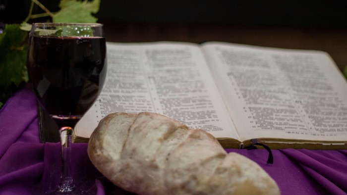 Wein, Brot und offenes Buch auf violettem Tuch