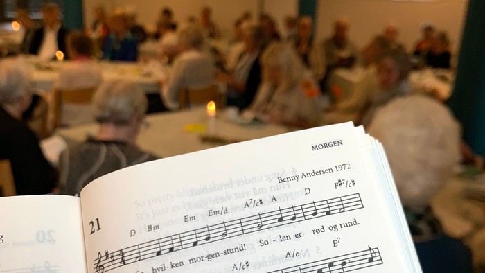 En gruppe af mennesker deltager i en sangstund med noter og lysede lygter.