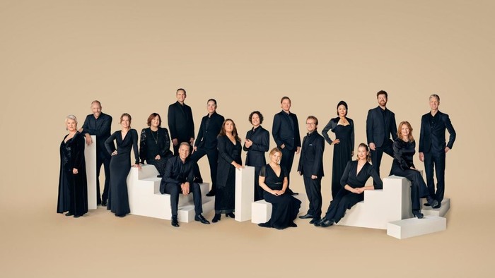 En gruppe musikere i formelt sort tøj, der poserer på moderne hvide platforme.