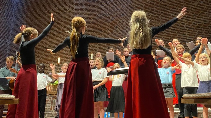 En gruppe kvinder i røde skørter og sorte topper danser på en scene foran en publikum.