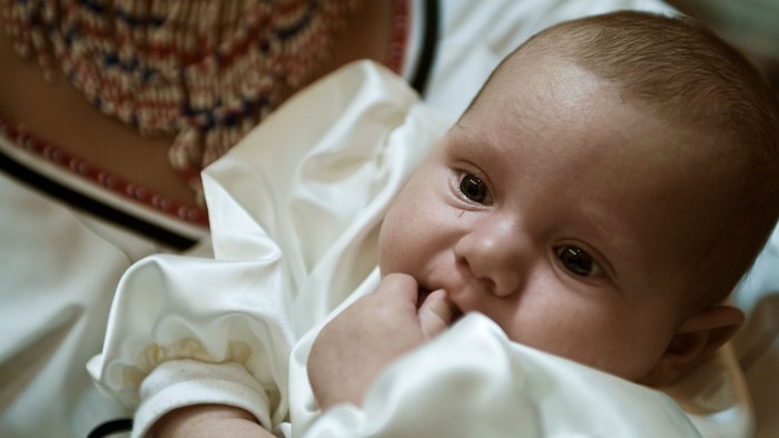 Et spæd barn ligger i en seng og ser op.