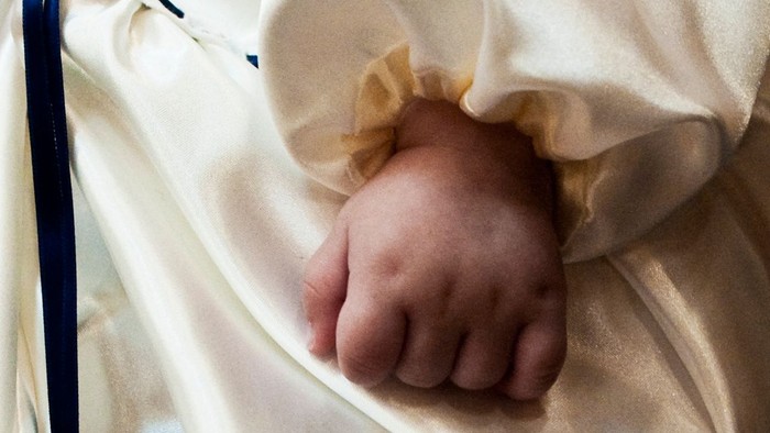 Et spæd barns hånd stikker ud af en hvid pude.