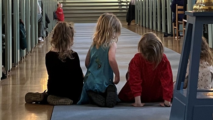 Tre børn sidder i en kirke.