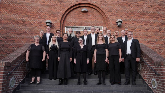 Gruppe af formelt klædte mennesker, der poser sammen foran en murstensvæg.