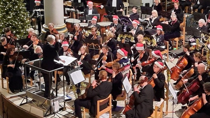 Orchestra performing on stage with conductor and musicians playing various instruments.