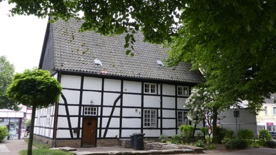 Das Bild zeigt ein traditionelles Fachwerkhaus mit einem steilen Dach und einem kleinen Vorgarten.