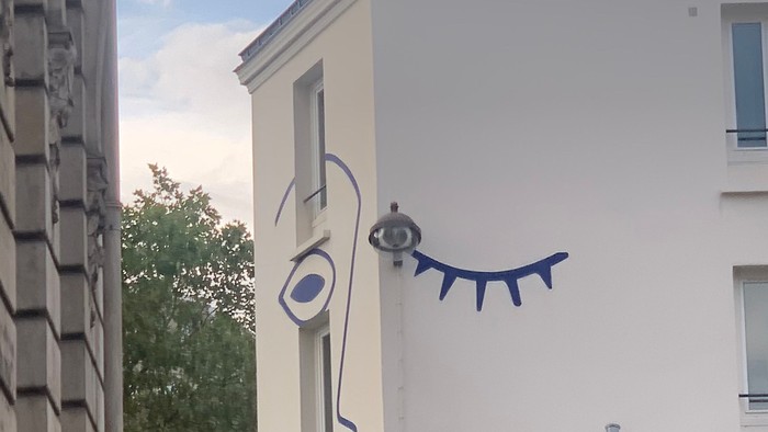 En blå og hvid tegnelse af et øje og en snak på siden af et hvidt bygning.