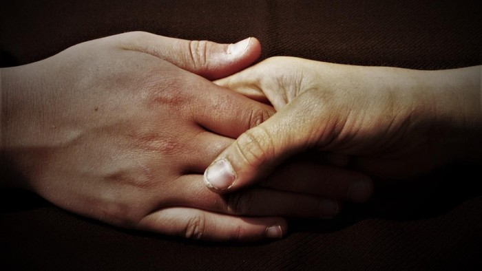 Zwei Hände, die sich halten, mit verschränkten Fingern.